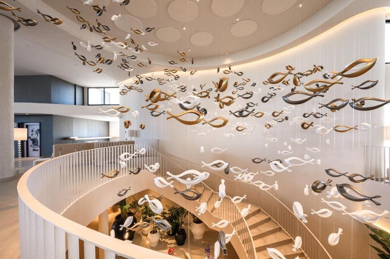 Un interior moderno con una escalera curva, detalles decorativos en el techo y una zona de estar con plantas.