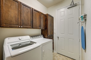 A laundry room with a front-loading washer and dryer, wooden cabinets above, and a white door with a towel hanging on the handle. - Olé at Lely Resort, More Than a Vacation (Naples)