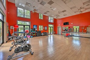 A gym with exercise equipment, large windows, and a red wall. - Olé at Lely Resort, More Than a Vacation (Naples)