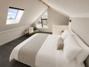 Ein Schlafzimmer mit einem großen Bett, einem Dachfenster, einem kleinen Tisch mit einer Pflanze und einem Sessel.
