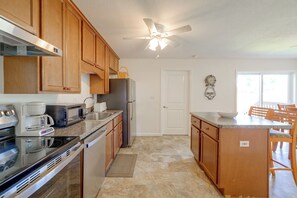 A kitchen with wooden cabinets, a refrigerator, a microwave, a coffee maker, a sink, and a dining area with chairs and a table. - Walk to Dining: Relax at 609 Gray (Wildwood)