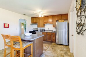 A kitchen with wooden cabinets, a stainless steel refrigerator, a microwave, and a dining area with a chair and a bowl. - Walk to Dining: Relax at 609 Gray (Wildwood)