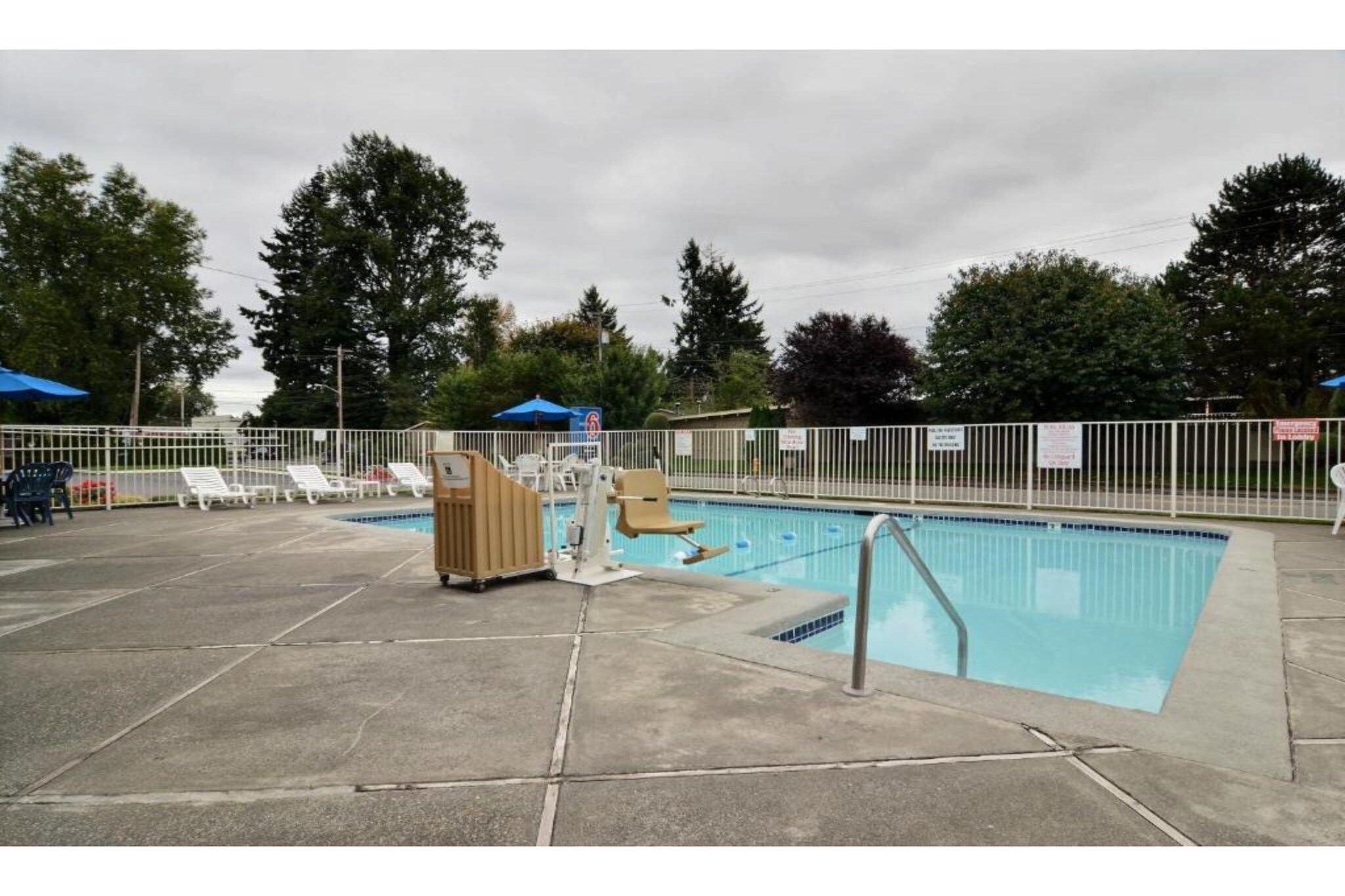 Ein Schwimmbecken mit Sprungbrett, Liegestühlen und einem eingezäunten Bereich.