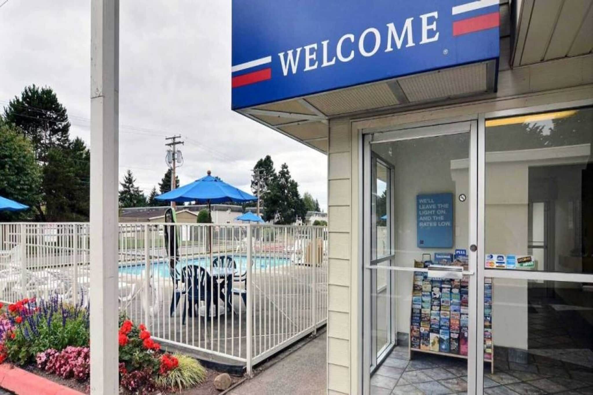 A welcome sign, a fenced pool area, and a building entrance with a magazine rack.