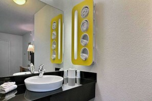 Ein Badezimmer mit einem weißen Waschbecken, einem Spiegel und einem gelben Handtuchhalter mit mehreren Ablagen.