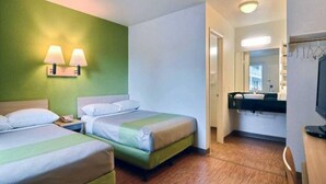 Habitación de hotel con dos camas, un baño con espejo y lavamanos, y un televisor.