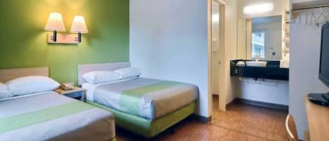 Una habitación de hotel con dos camas, un baño con espejo y una televisión.