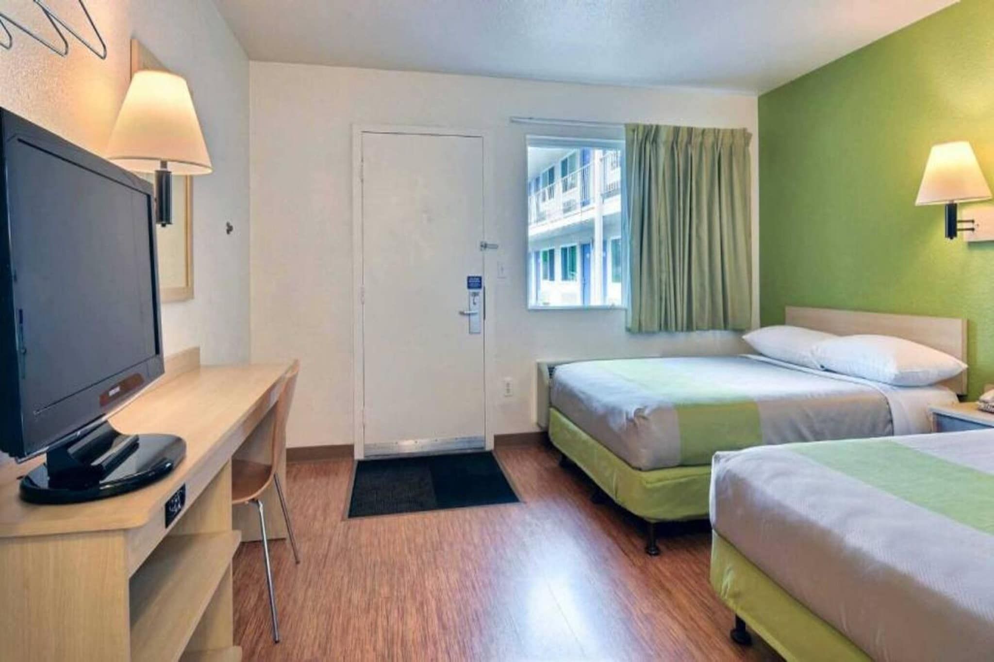 A hotel room with a desk, two beds, a television, and a window with curtains.