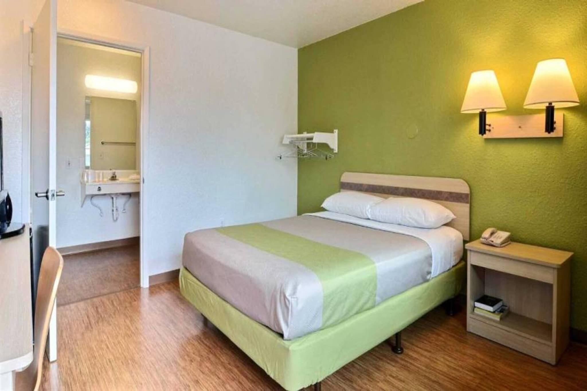 A hotel room with a bed, bedside table, lamp, and a mirror.