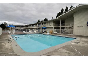 A swimming pool with lounge chairs and umbrellas, surrounded by a fenced area with a multi-story building in the background. - 1 Queen Bed | Non-Smoking, Mini Fridge (Tumwater)