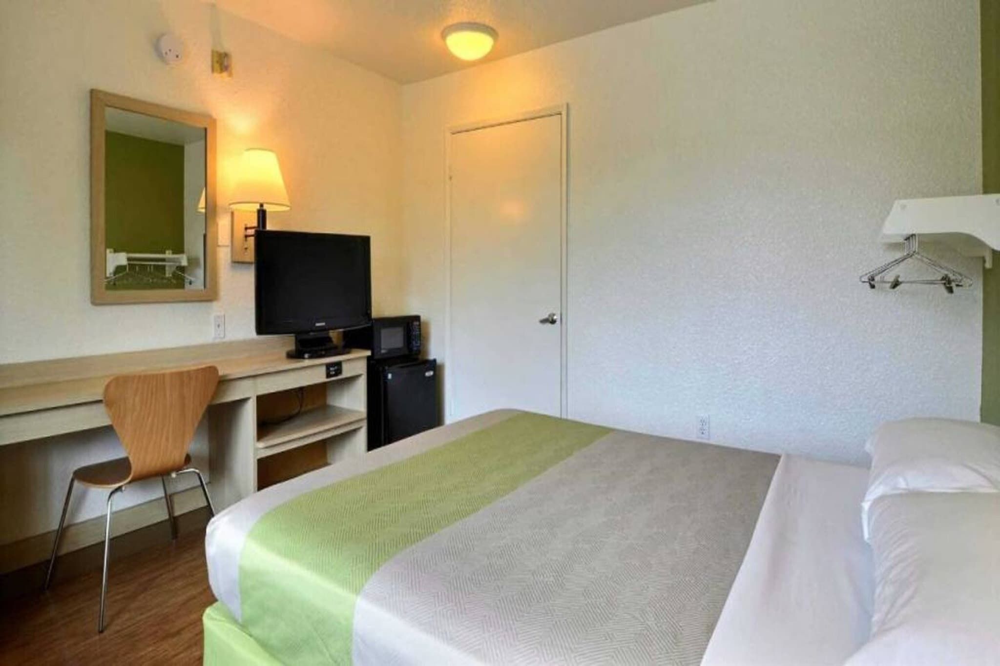 A hotel room with a bed, a desk with a computer, a chair, and a television.