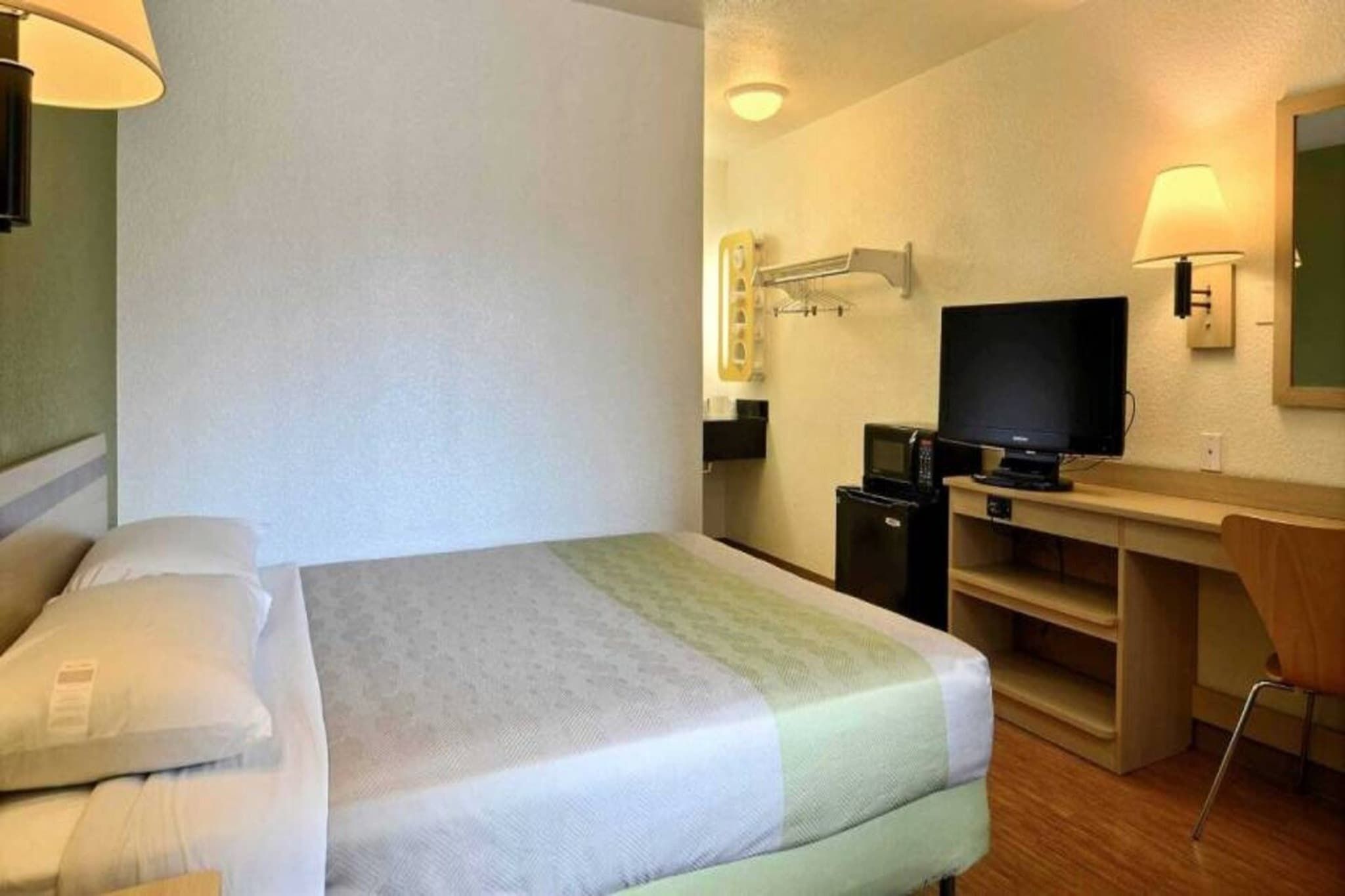 A hotel room with a bed, a desk, a television, and a microwave.