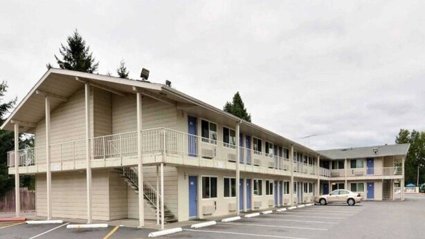 Un motel con una estructura de dos pisos, una zona de estacionamiento techada y un edificio de un piso contiguo.