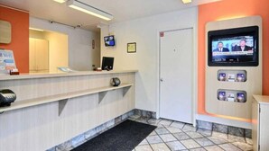 Zona de recepción con mostrador, pantalla de televisión, una puerta y un pequeño estante con objetos.