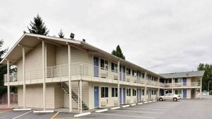 Un motel con una estructura de dos pisos, una zona de estacionamiento techada y un edificio de un piso adyacente.