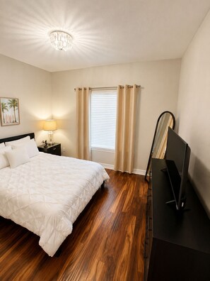 A bedroom with a bed, a nightstand, a lamp, a window with curtains, a mirror, and a television. - Peaceful studio with AC in charming Cape Coral & seasonal pool and jacuzzi (Cape Coral)