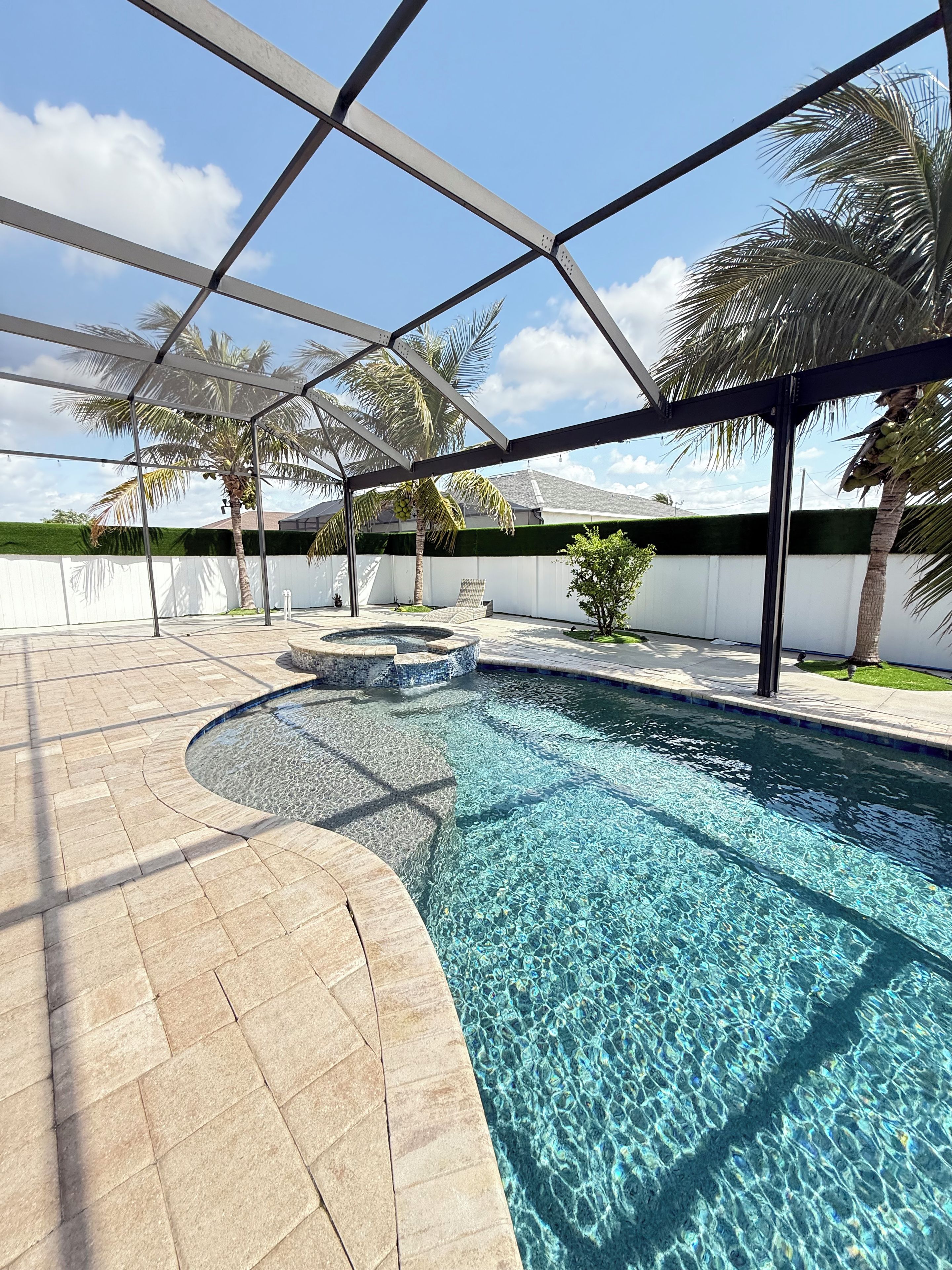 A swimming pool with clear water, surrounded by a paved deck and palm trees.