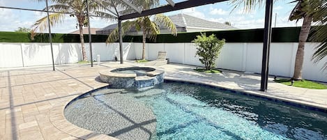A swimming pool with clear water, surrounded by a paved deck and palm trees.
