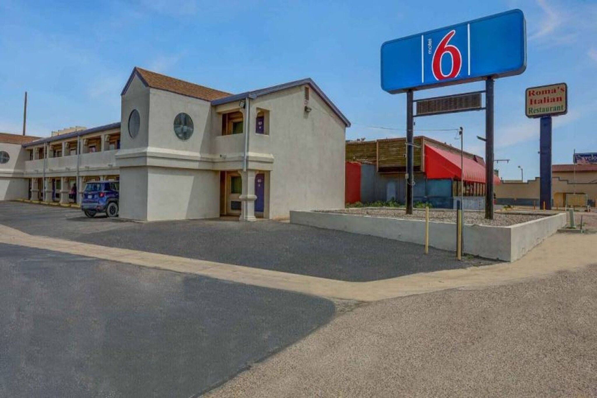 Un motel con un llamativo letrero con el número '6', un estacionamiento y un edificio con toldo rojo.