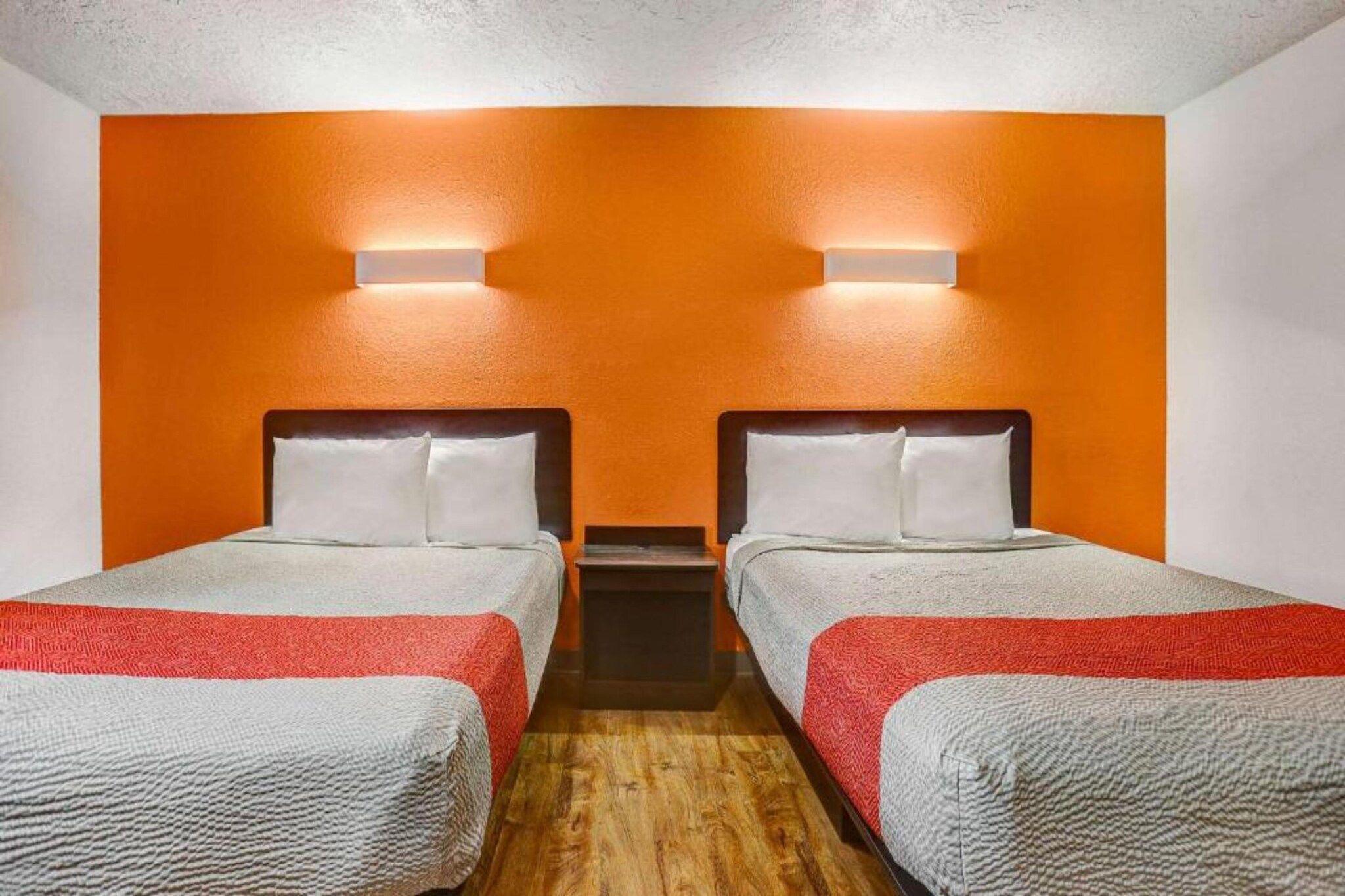 Ein Hotelzimmer mit zwei Betten, jeweils mit Kopfstütze, Nachttisch und Wandlampe.