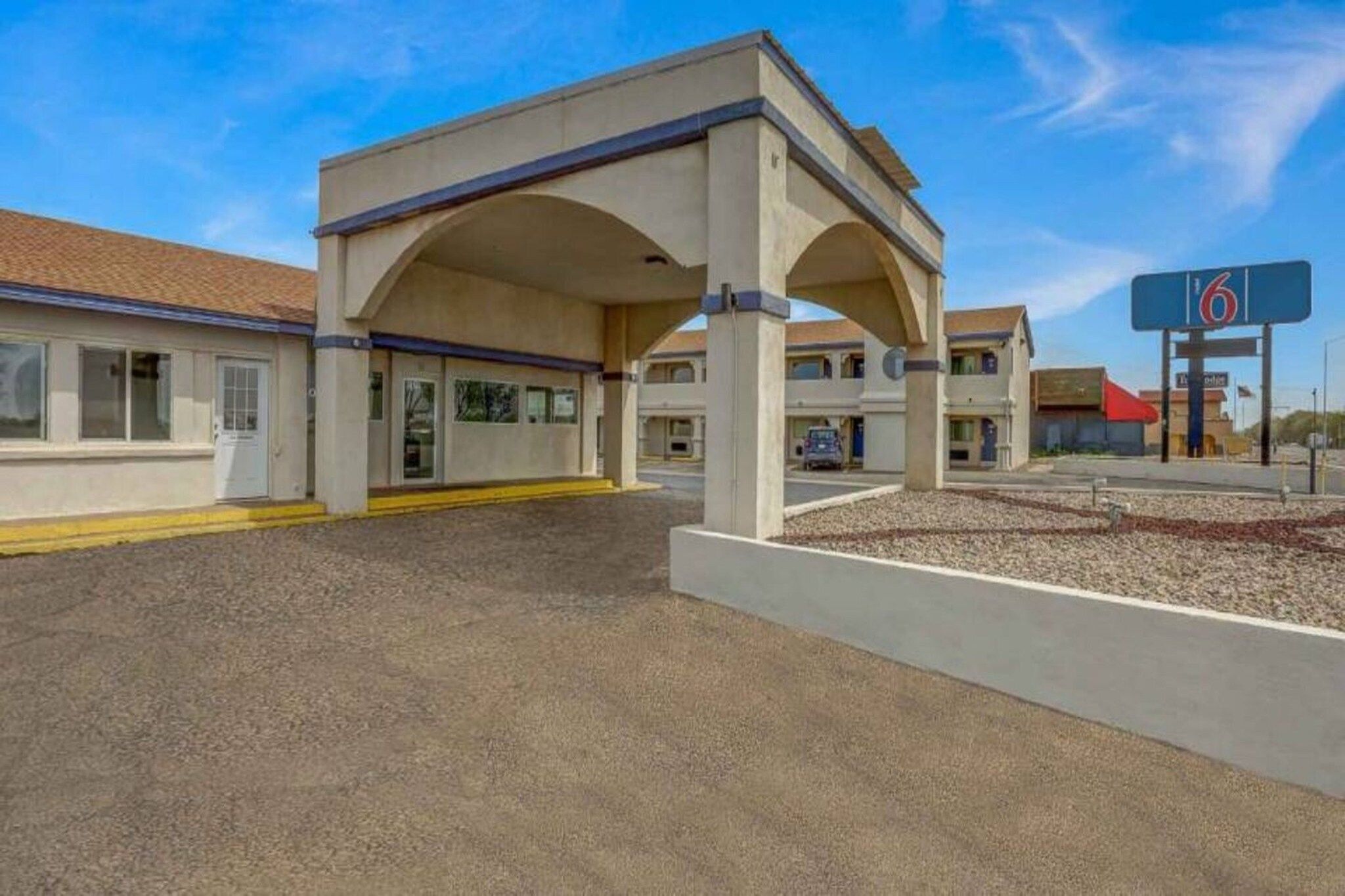 Un motel doté d’un parking couvert, d’un panneau indiquant une station-service et offrant une vue sur un ciel dégagé.