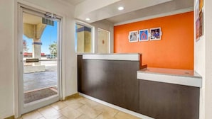 A reception area with a glass door entrance, a counter with a dark panel, and a wall with framed pictures. - 2 Queen Beds | Non-Smoking (Clovis NM)