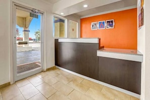 A reception area with a glass door entrance, a counter with a dark panel, and a wall with framed pictures. - 2 Queen Beds | Non-Smoking (Clovis NM)