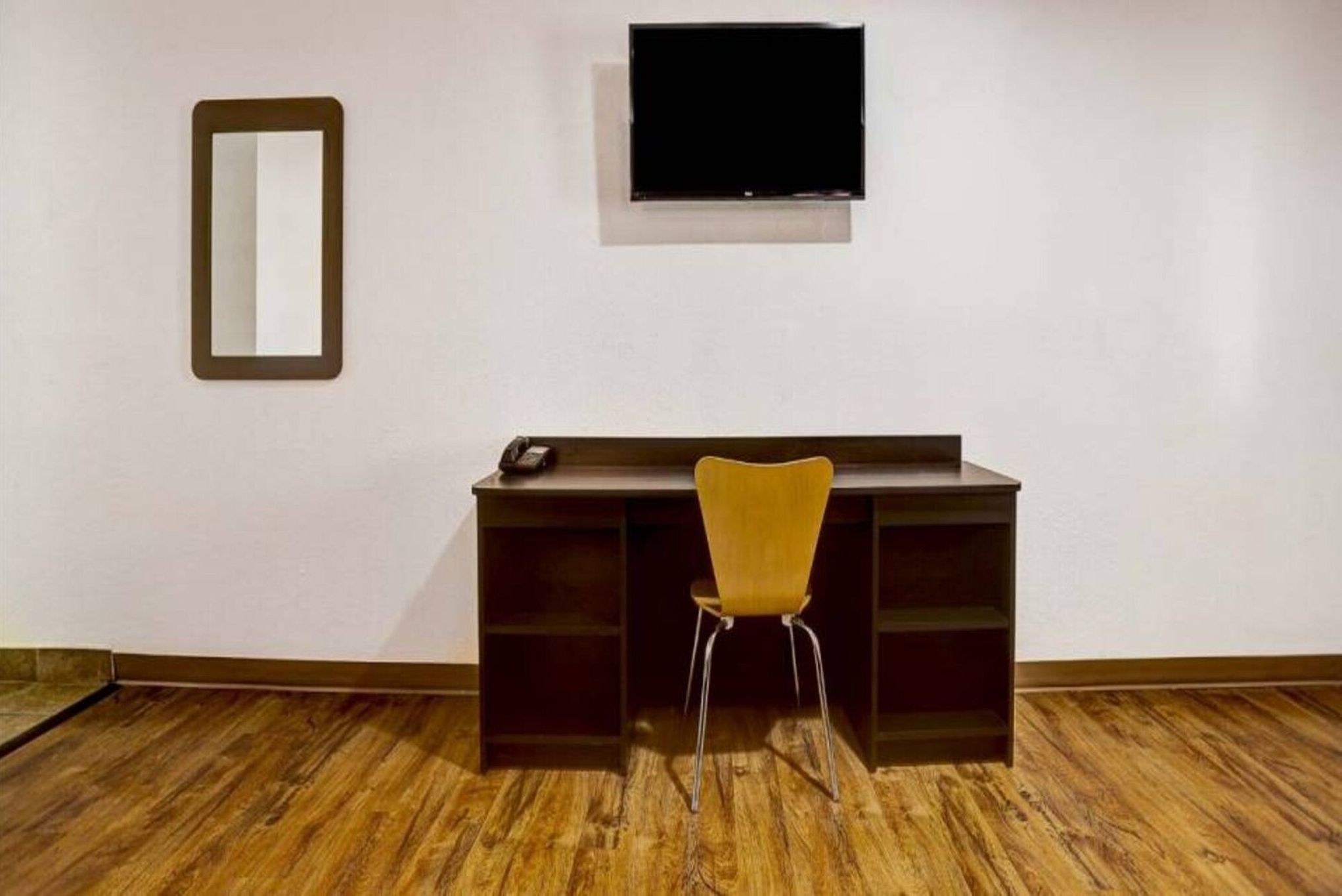 Una habitación con escritorio, silla, televisor montado en la pared y espejo.