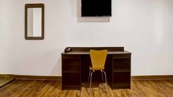 Una habitación con escritorio, silla, televisor montado en la pared y espejo.