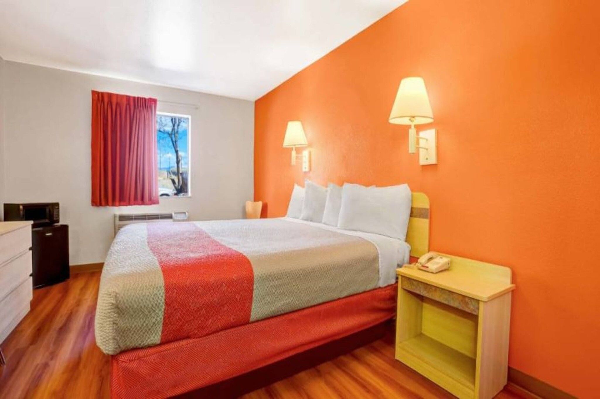 Una camera d'albergo con un letto, un comodino, una lampada e una finestra con tende.