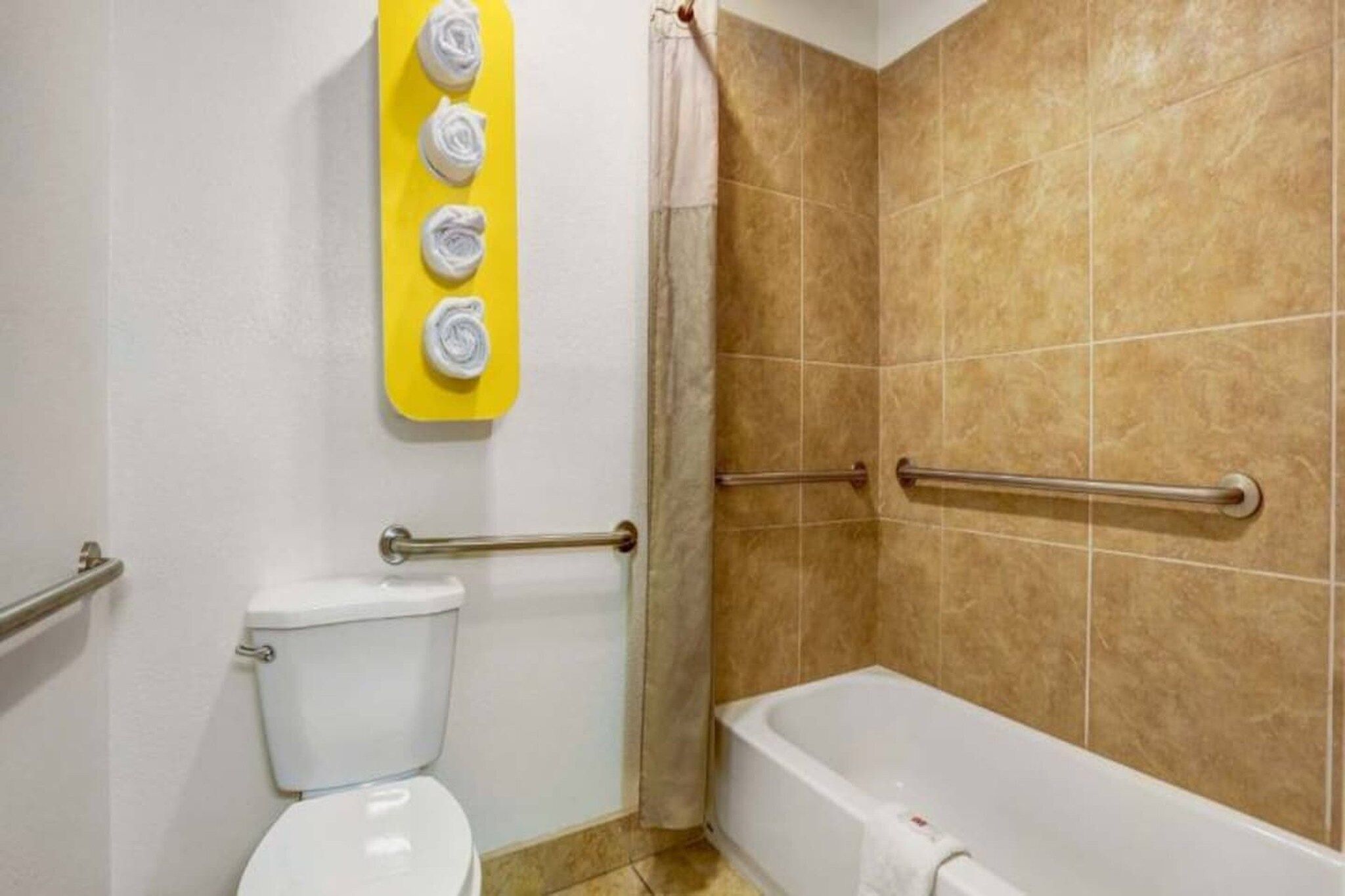 A bathroom with a toilet, a bathtub, and a shower area with grab bars.