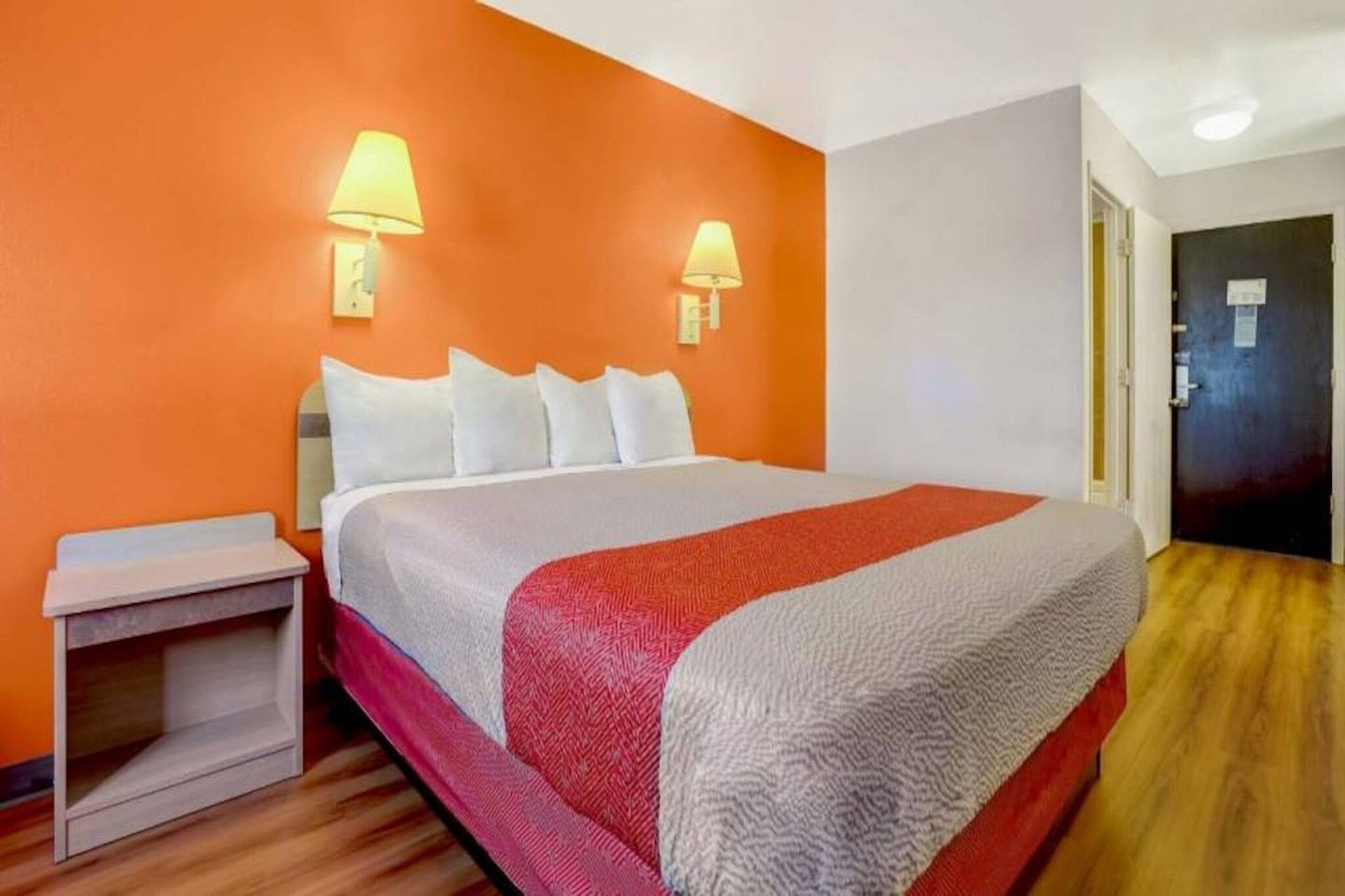 A hotel room with a bed, nightstand, and two wall-mounted lamps.