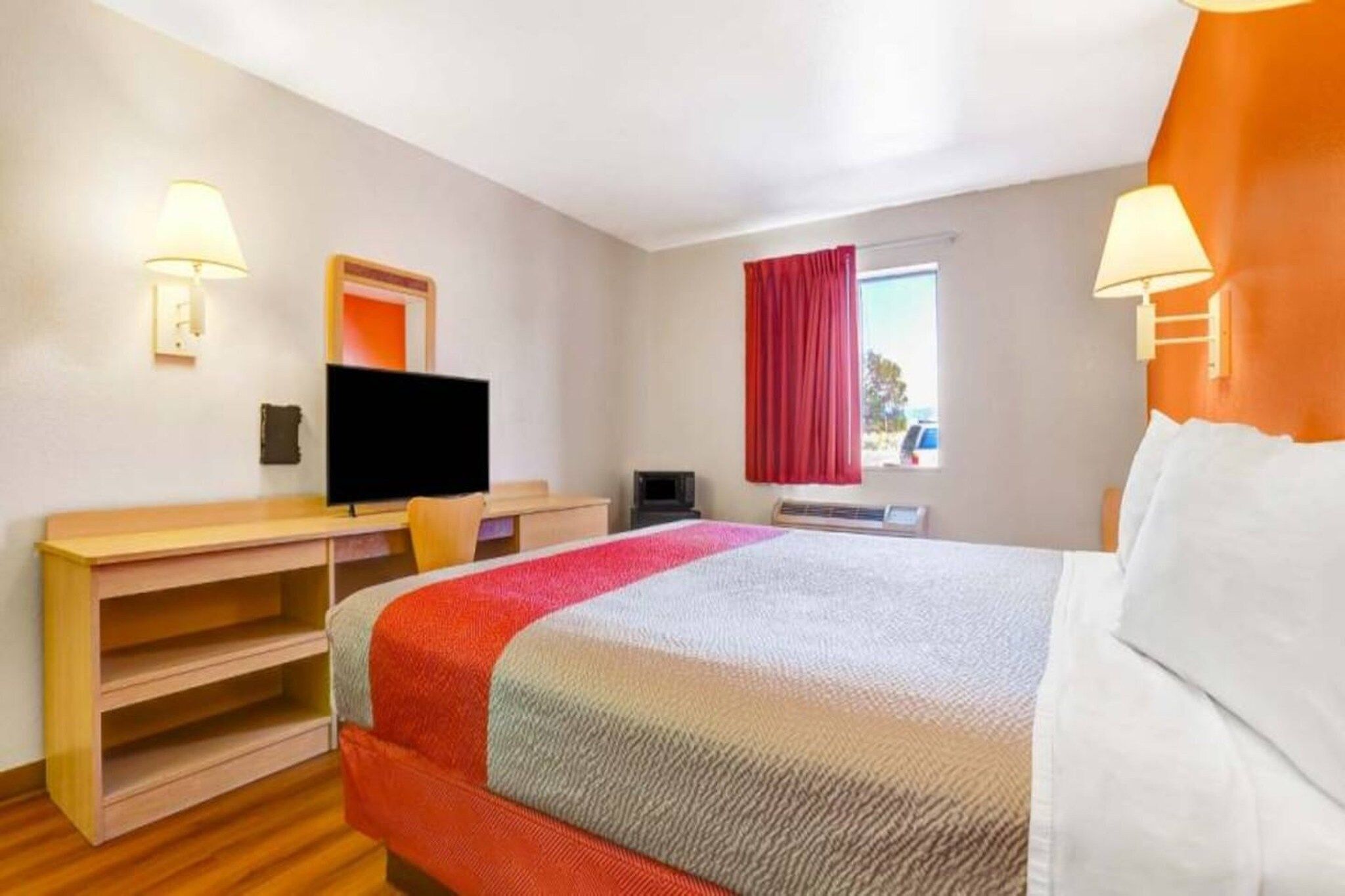 Ein Hotelzimmer mit Bett, Schreibtisch, Fernseher und einem Fenster mit Vorhängen.