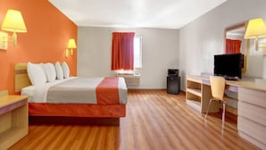 Quarto de hotel com cama, escrivaninha, cadeira, televisão e janela com cortinas.