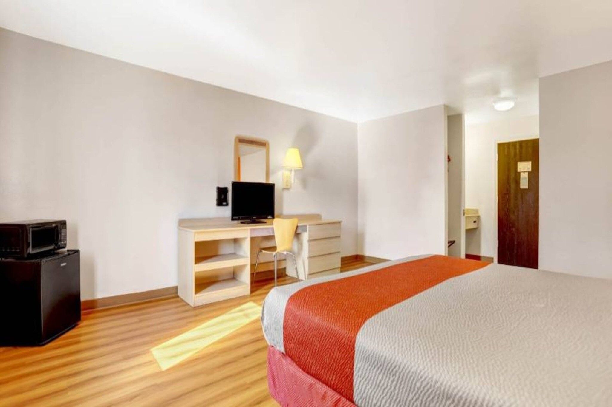 A hotel room with a bed, a desk, a chair, a television, and a refrigerator.