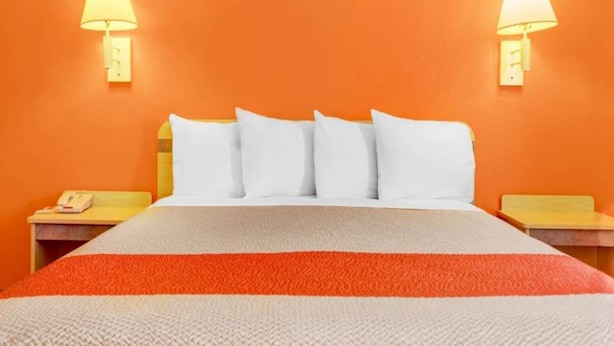 Cama com almofadas brancas, manta listrada em vermelho e branco e duas luminárias de cabeceira em paredes laranja.