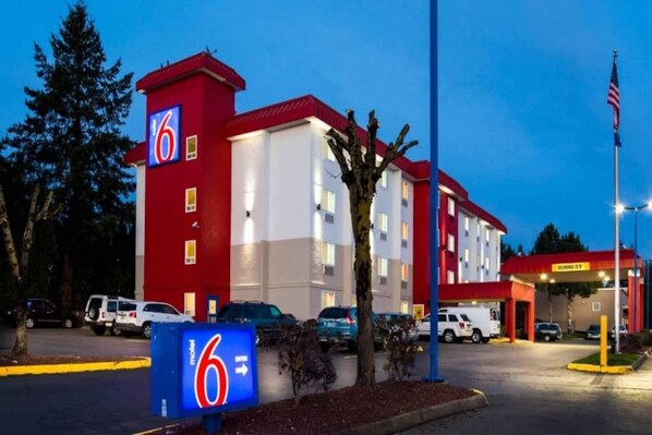 Ein Motel mit roter und weißer Fassade, ein Parkplatz mit mehreren Autos und ein Schild mit dem Namen des Motels.