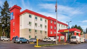 Un hotel de varios pisos con fachada roja y blanca, una estación de servicio y varios autos estacionados.
