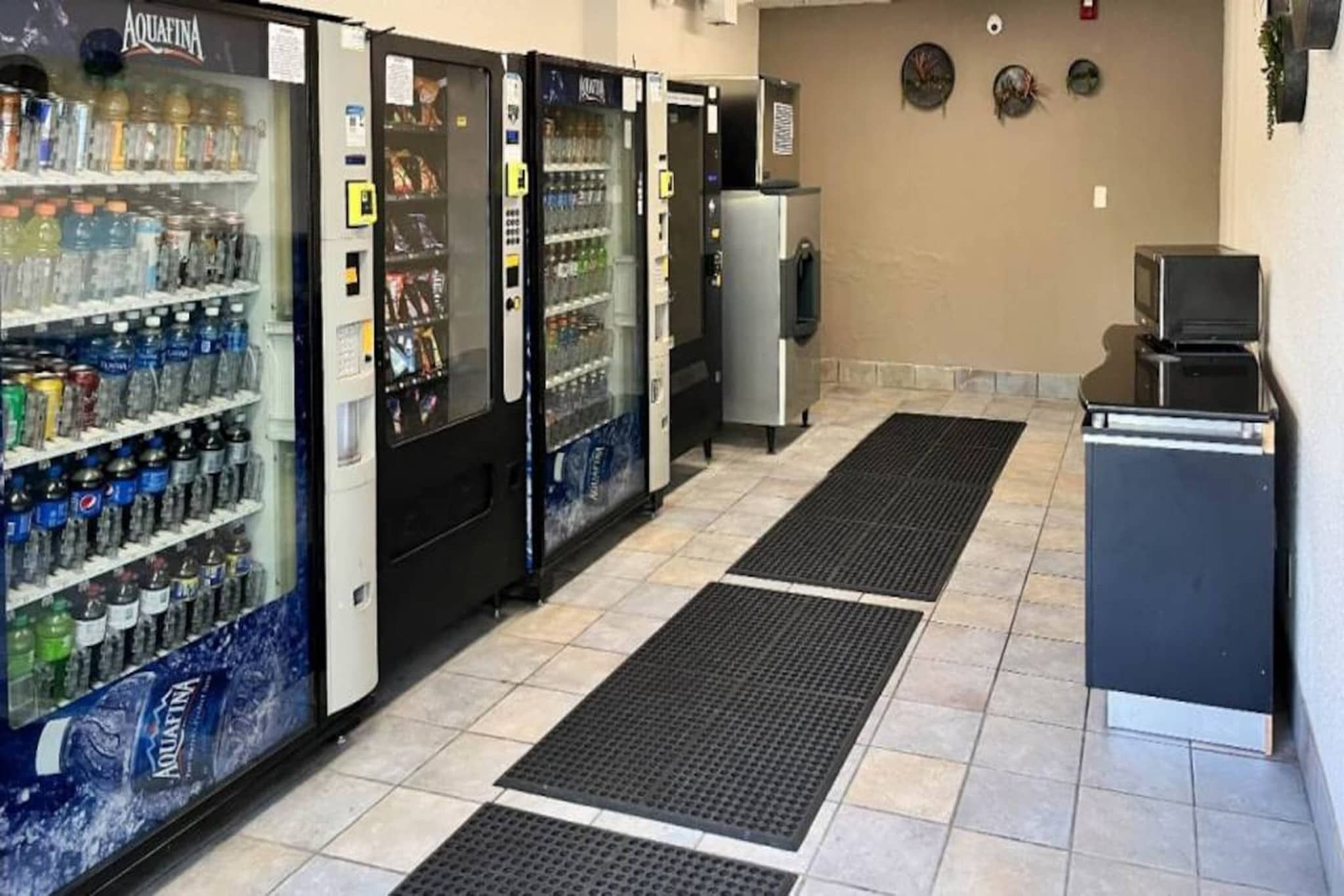 A row of self-service beverage dispensers with various drink options, a small refrigerator, and a microwave.
