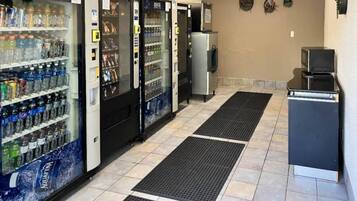 A row of self-service beverage dispensers with various drink options, a small refrigerator, and a microwave.
