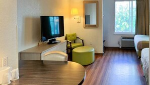 Una habitación de hotel con televisión, una silla verde, una mesa redonda y una cama.
