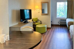 Ein Hotelzimmer mit Fernseher, einem grünen Sessel, einem runden Tisch und einem Bett.