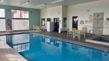 Una piscina interior con agua cristalina, rodeada de sillones de descanso y un suelo de baldosas.