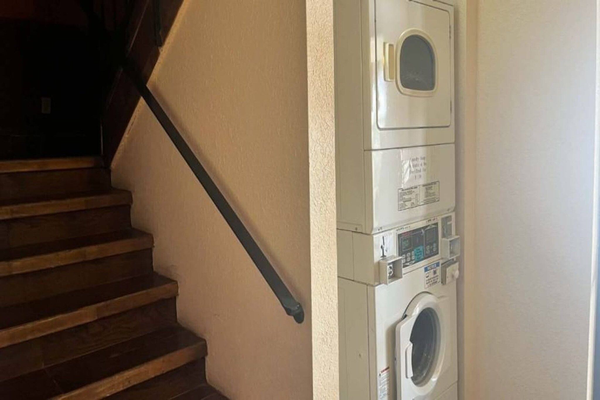 Un lavadero con lavadora y secadora, una escalera de madera y una pared blanca.