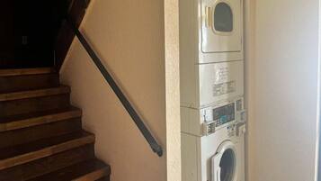 A laundry room with a washing machine and dryer, a wooden staircase, and a white wall.