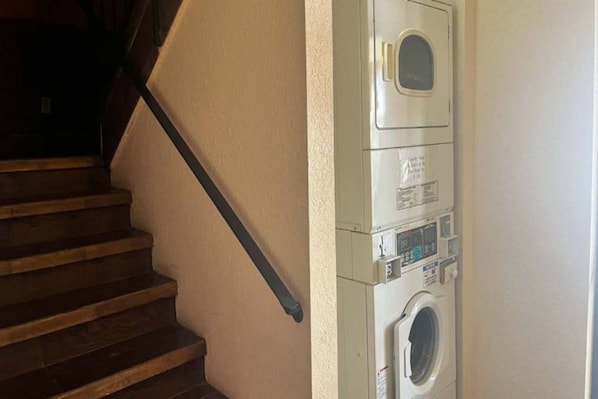 A laundry room with a washing machine and dryer, a wooden staircase, and a white wall.