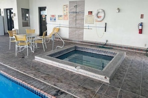 A swimming pool with a tiled deck, a seating area with chairs, and safety signs on the walls.