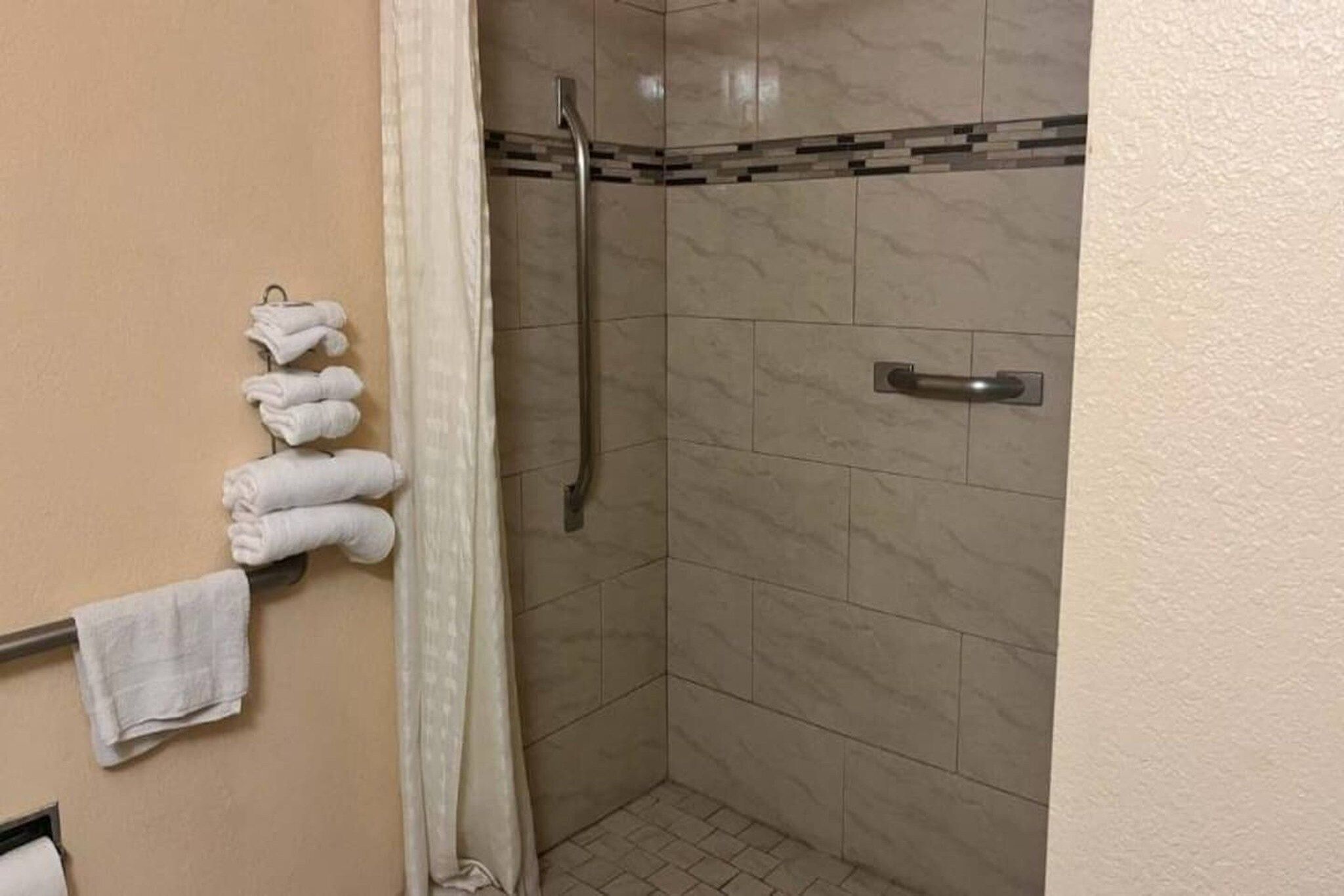A bathroom with a shower stall, a towel rack with folded towels, and a shower curtain.