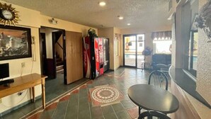 A hotel lobby with a reception desk, a seating area with a table and chairs, a Coca-Cola refrigerator, and a large window. - 2 Queen Beds | Non-Smoking, Micfridge (Deming NM)