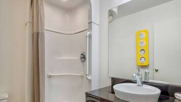 Un baño moderno con ducha a nivel, un lavabo con espejo y un dispensador de jabón amarillo.
